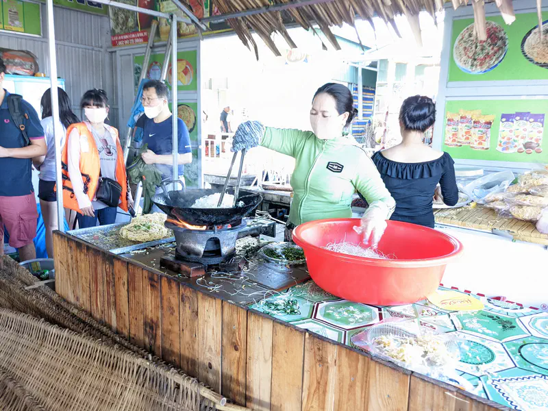 Woman making thin rice paper sheets on a steaming pan.