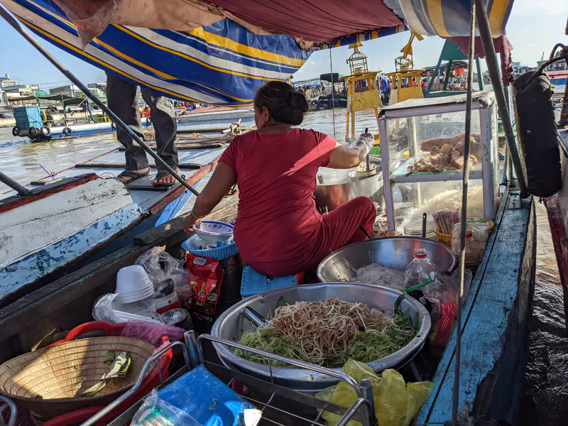 Vendor preparing noodle soup on a small boat kitchen at Cai Rang floating market.