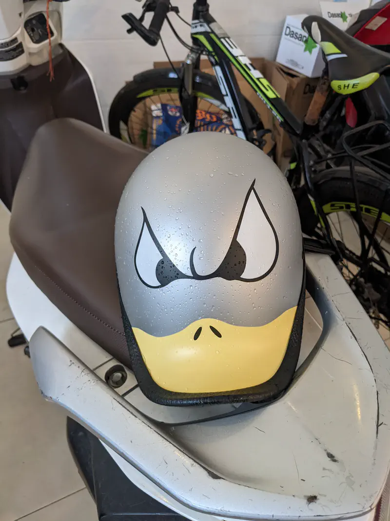 Motorbike helmet with a cartoon duck face design, featuring angry eyes and a yellow beak.
